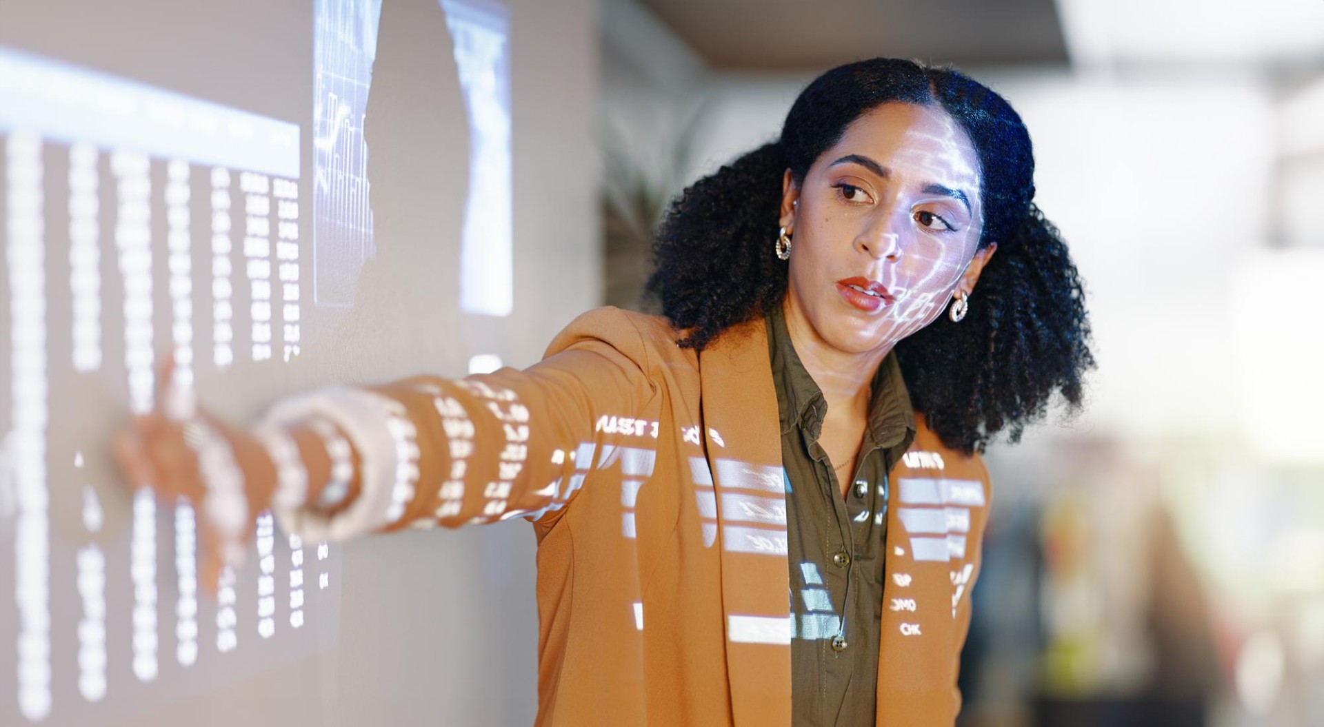 Student in professional tan jacket points at projection screen while making a class presentation
