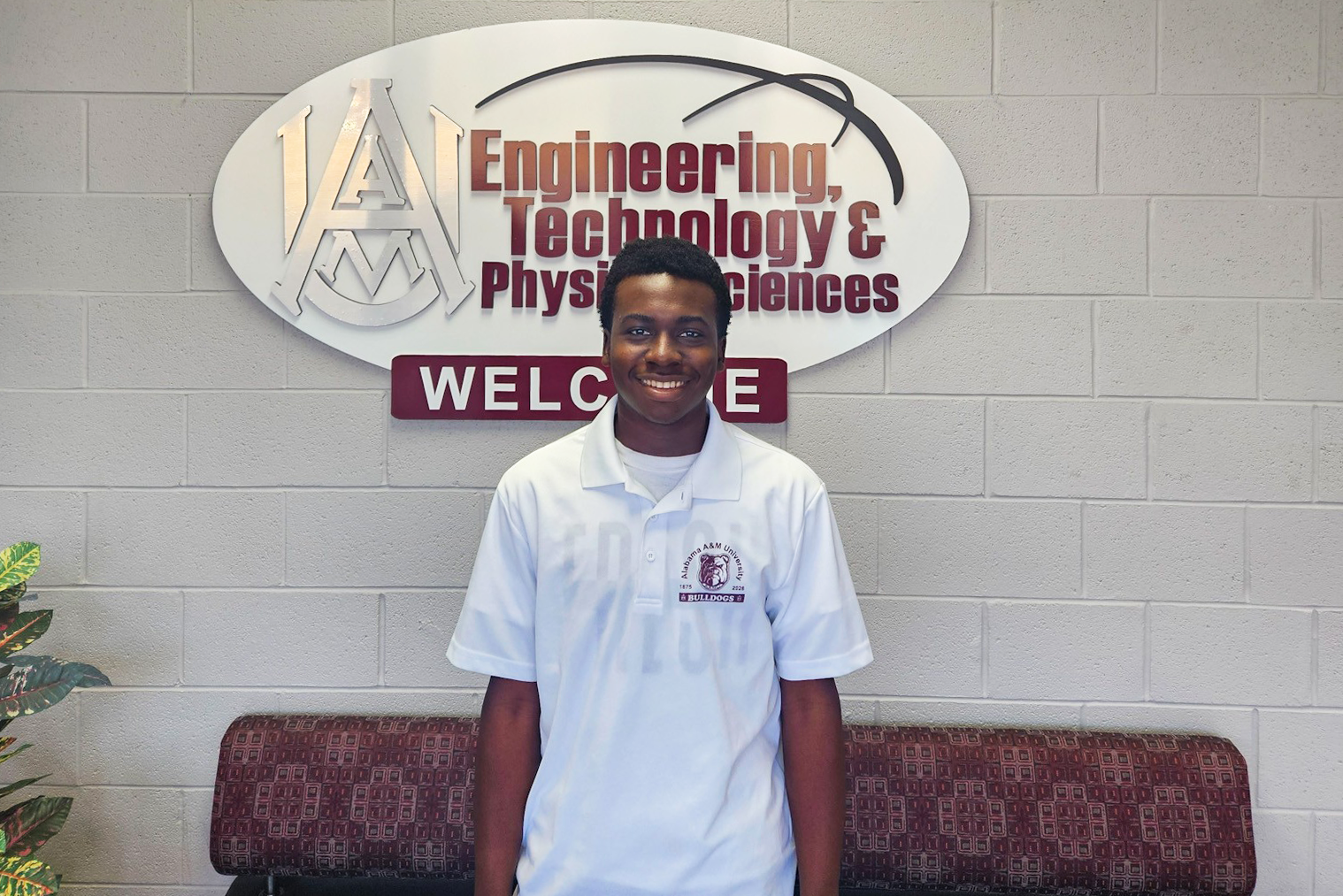 Adeyori Adekunle smiles in front of Engineering, Technology & Physical Sciences sign in AAMU's Bond Hall