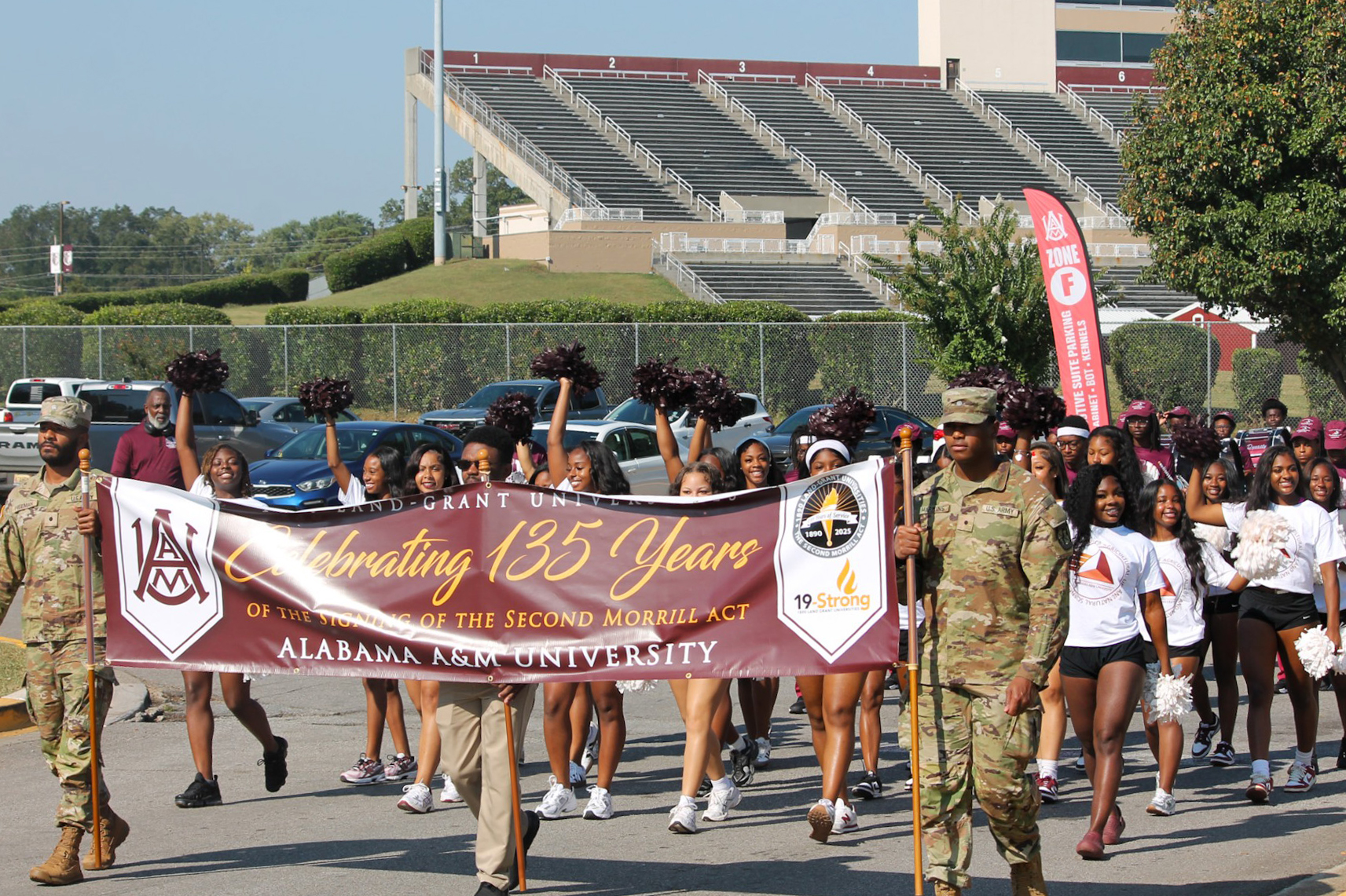 AAMU ROTC members hold flag commemorating 135th Anniversary of Second Morrill Act with students behind them at start of march from Louis Crews Stadium