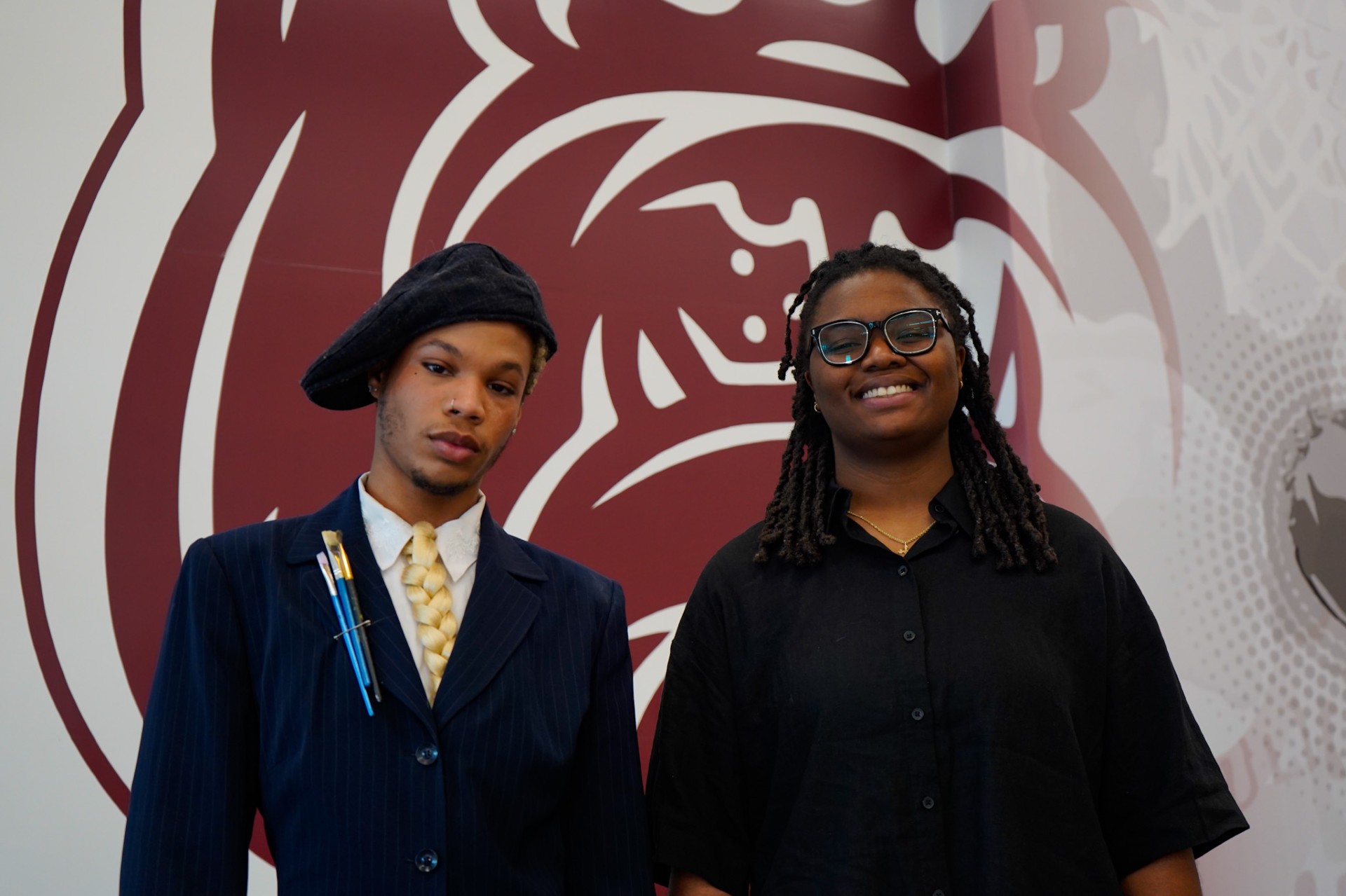 Quentell Pentecost and Somara Butchers stand in front of Bulldog on the wall of the Event Center