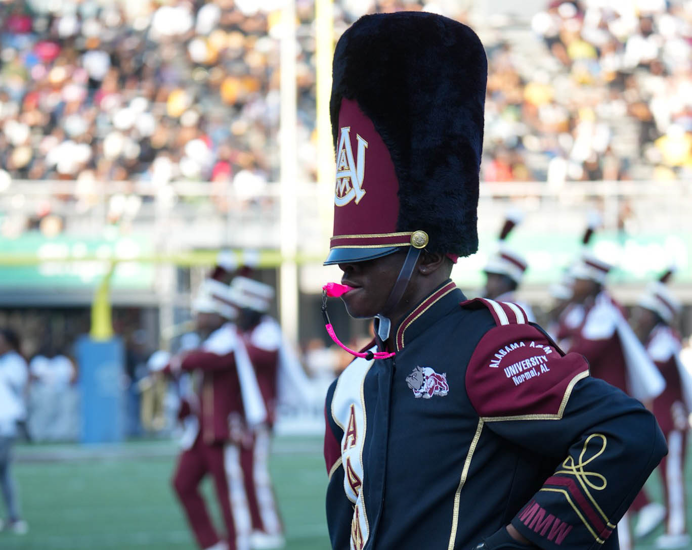 Tight shot of drum major with whistle in mouth and five AAMU band members marching behind him during football game performance
