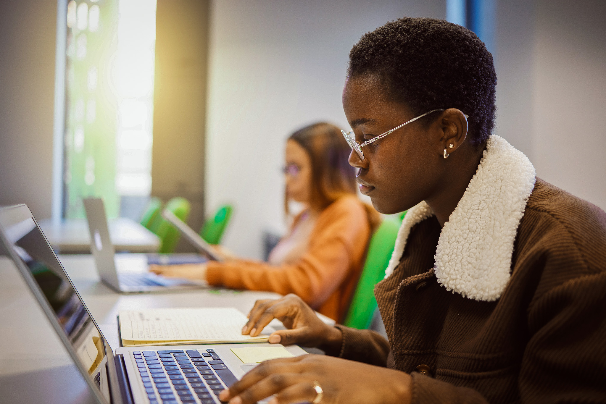 Student working on computer with another student in the background