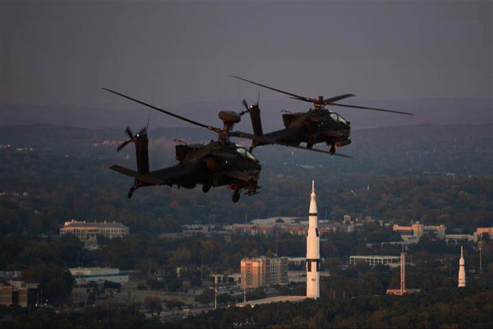Two RTC Apache helicopters fly over Huntsville at dusk above the rocket at the U.S. Space & Rocket Center
