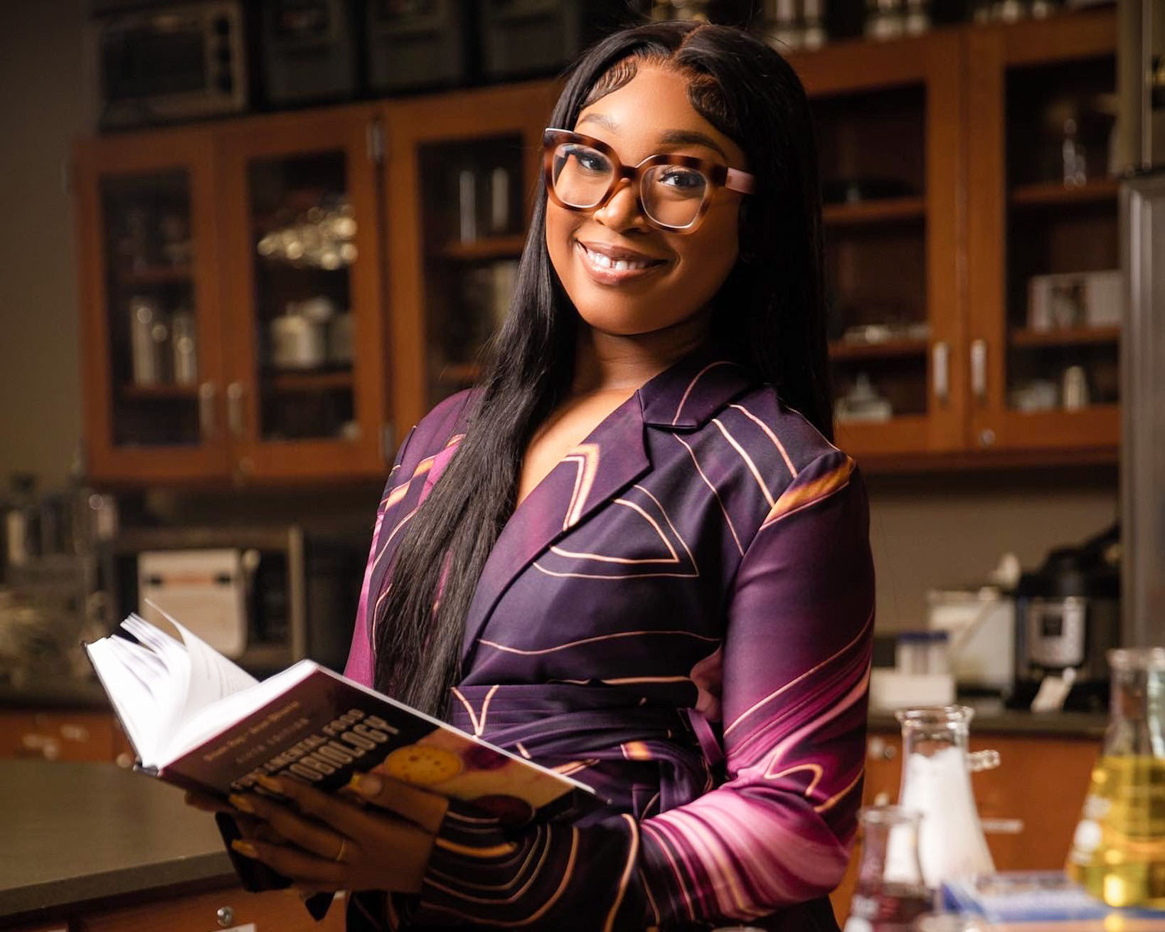 Jailyn Leonard holds a book surrounded by science beakers in the AAMU library