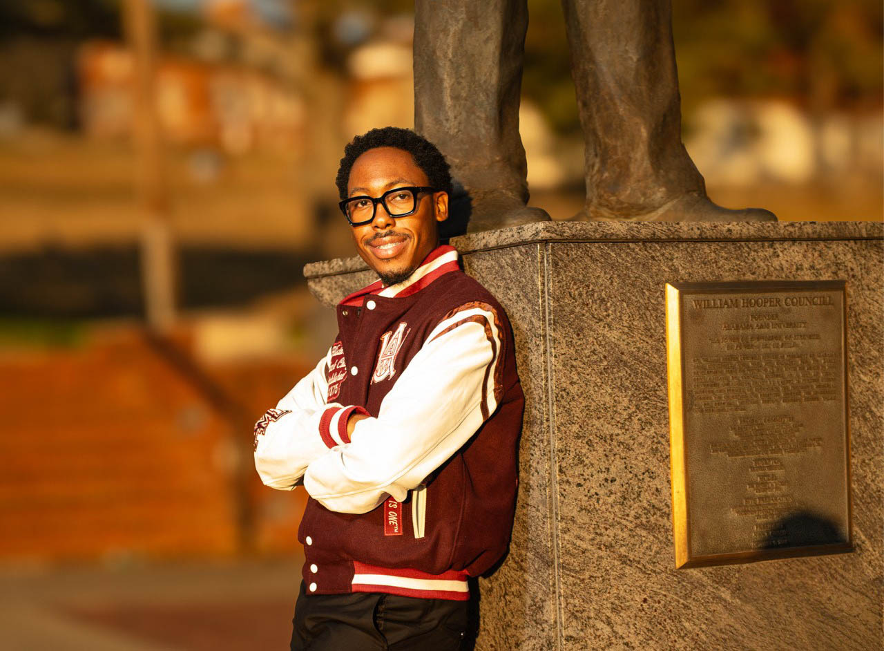 Donovan Horne wears an AAMU jacket and stands at the foot of the William Hooper Councill statue at Alabama A&M University