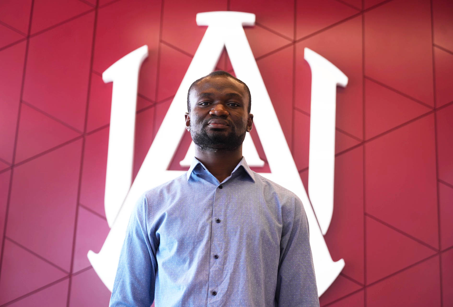 Ghanian Pir Entrepreneur Francis Adeina Stands in front of the AAMU Interlock Logo at the Event Center