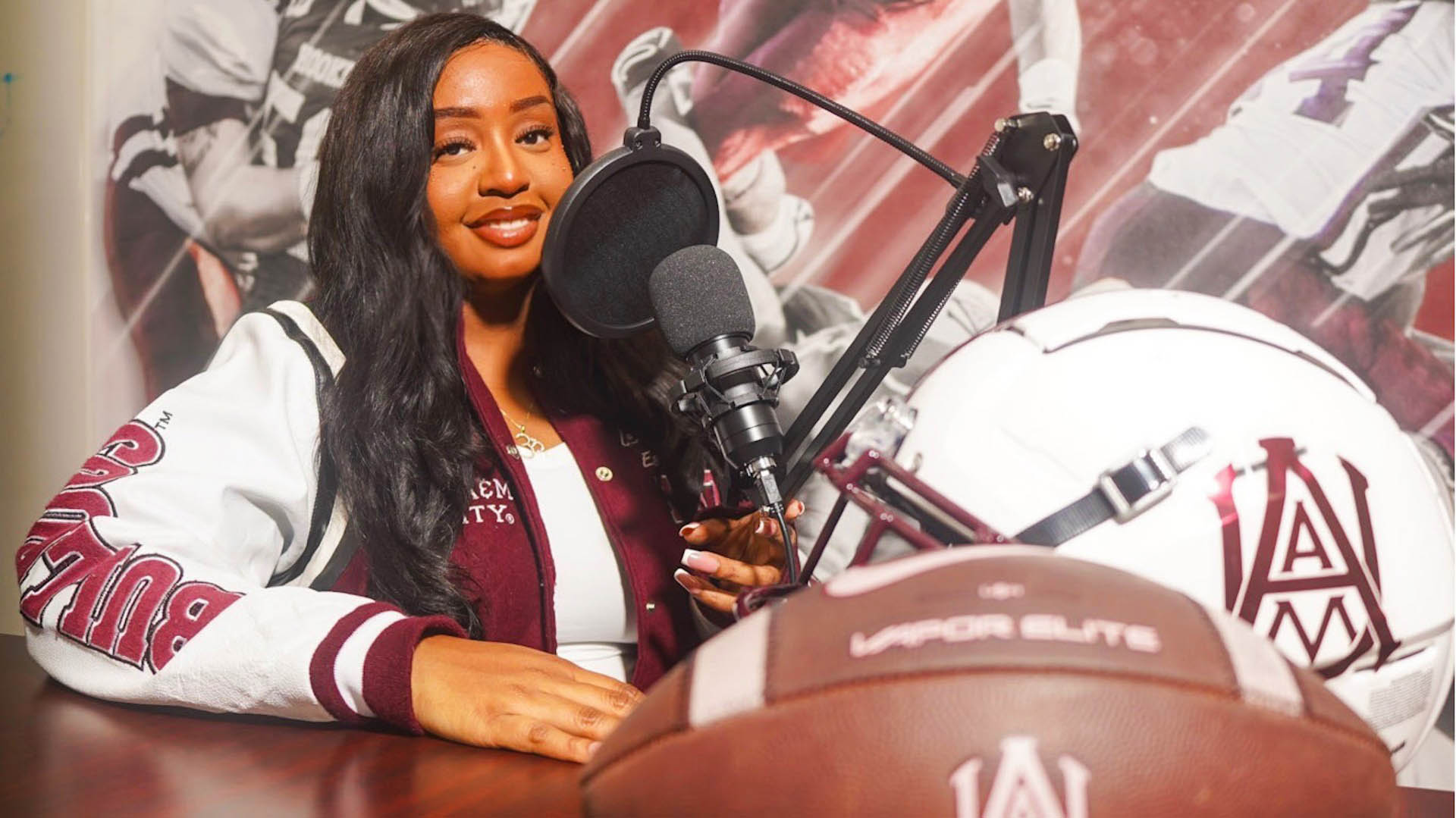 Thai Floyd wears AAMU jacket in front of a microphone and an AAMU football