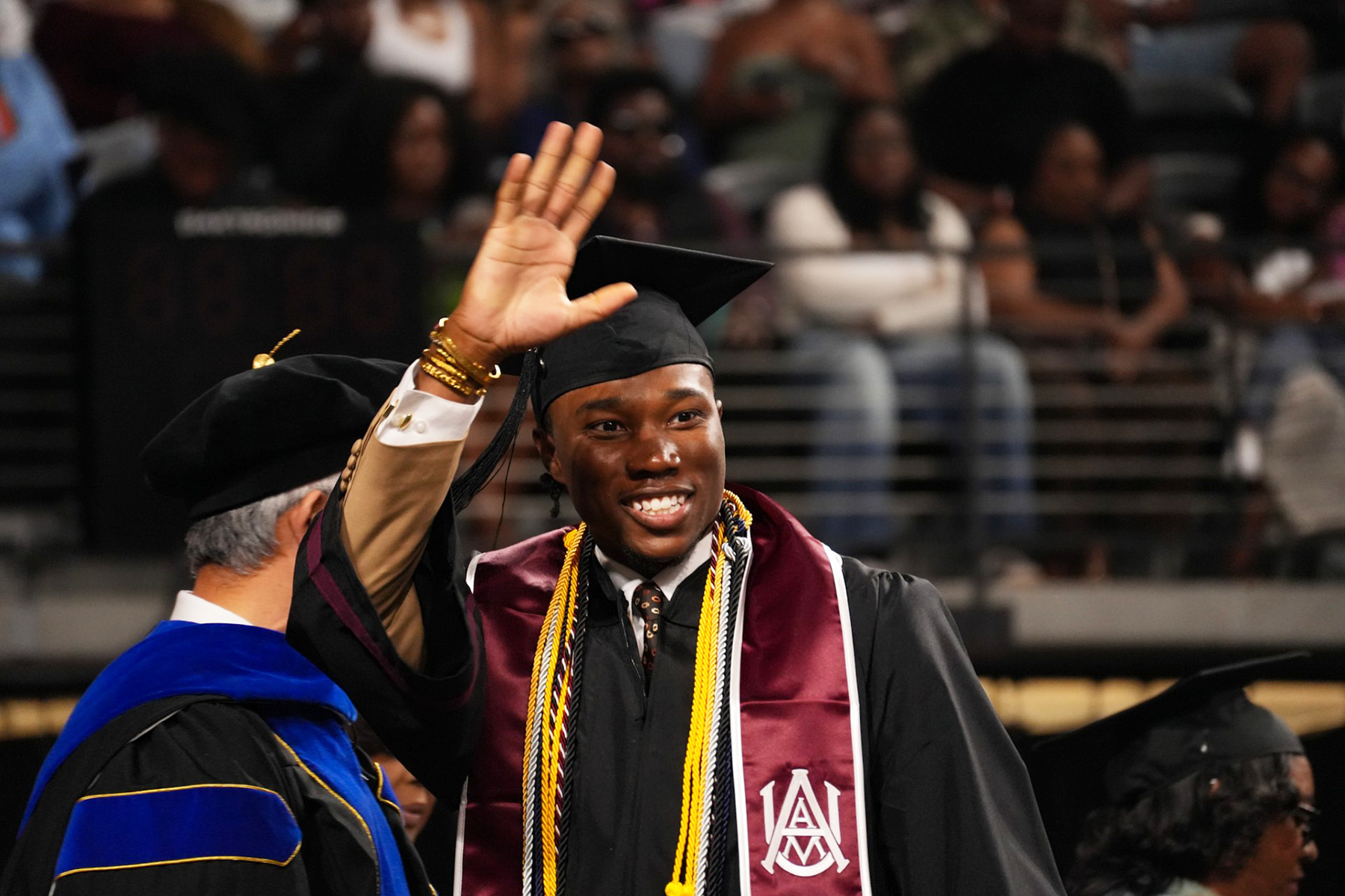 AAMU graduate smiles and waves as he crosses the stage
