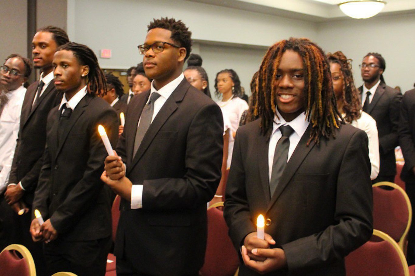 Male Honors Scholar holding candle along with several next to him and behind him