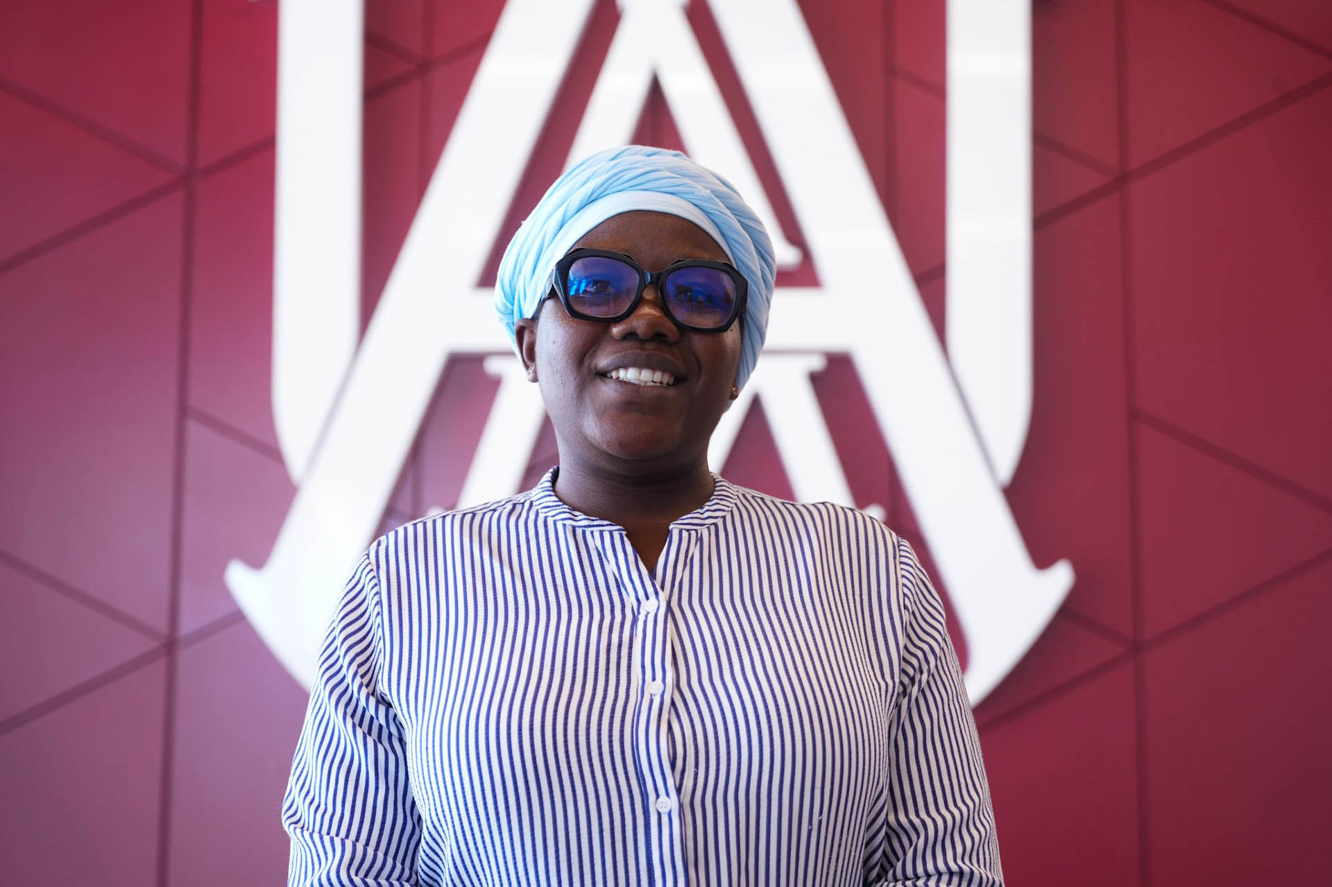 Jelila Seho Blalogoe smiles in front of the AAMU Interlock Logo at the Event Center