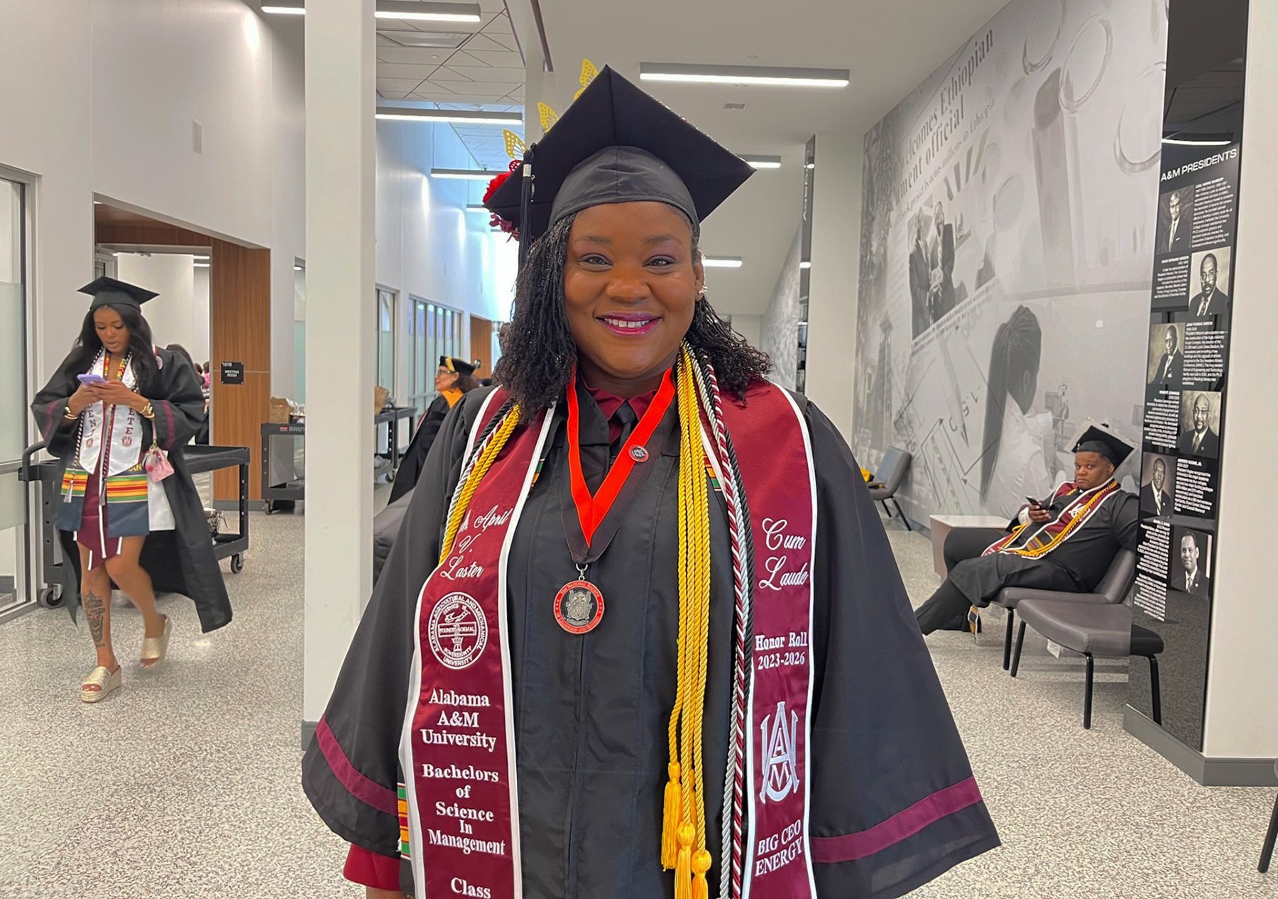 April Laster smiles wearing her regalia and honors sash in the AAMU Event Center