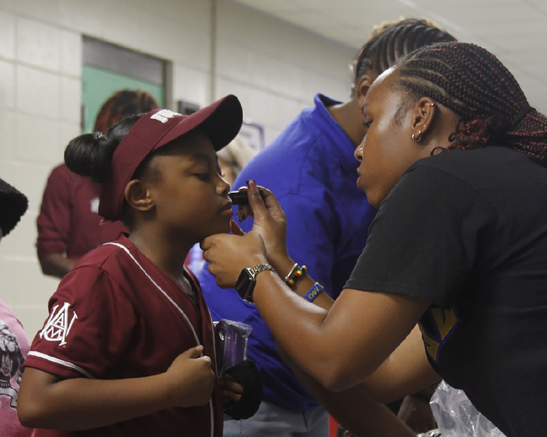 Alabama A&M University student and volunteer Karley Brazil paints a student’s face during the Bulldog Pregame Rush at MLK Elementary School.