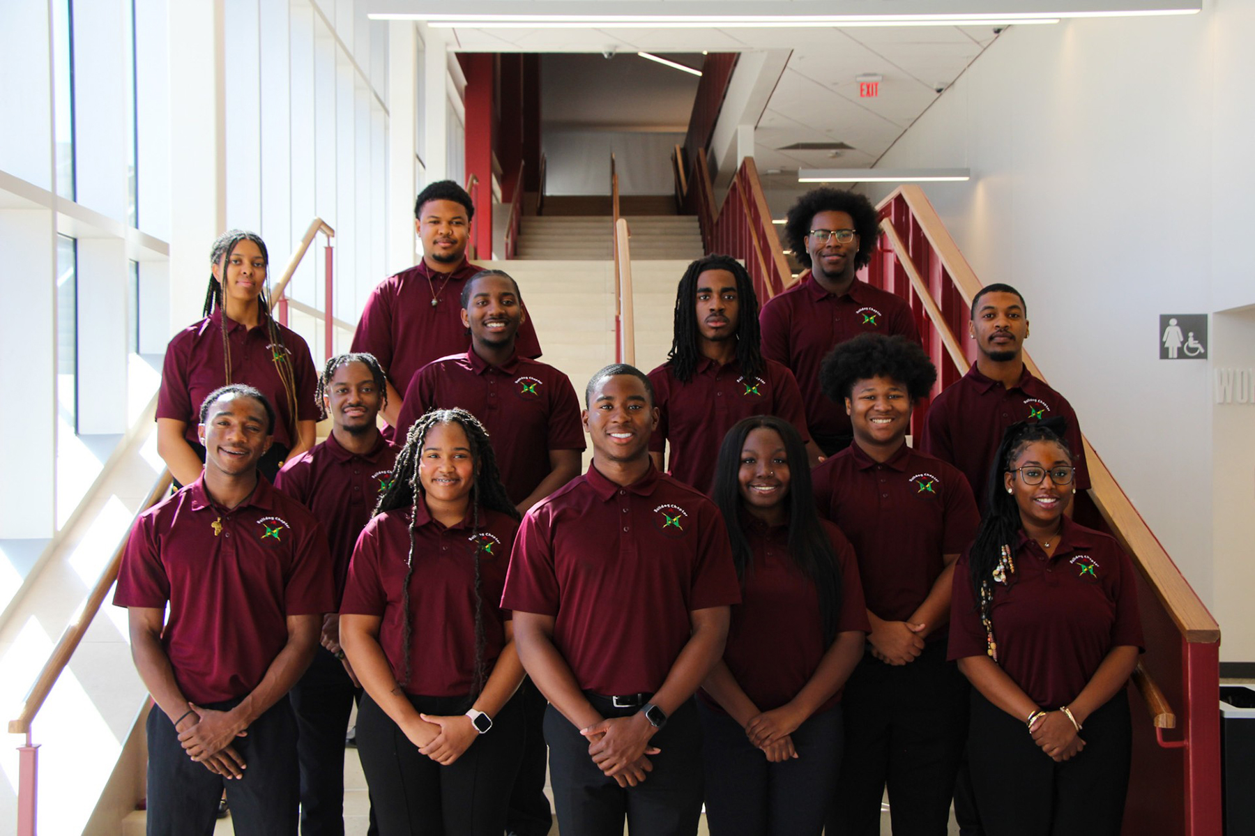 13 members of AAMU's Bulldog Chapter of the National Association of Black Engineers wear matching shirts and smile on the stairs in the AAMU Event Center lobby