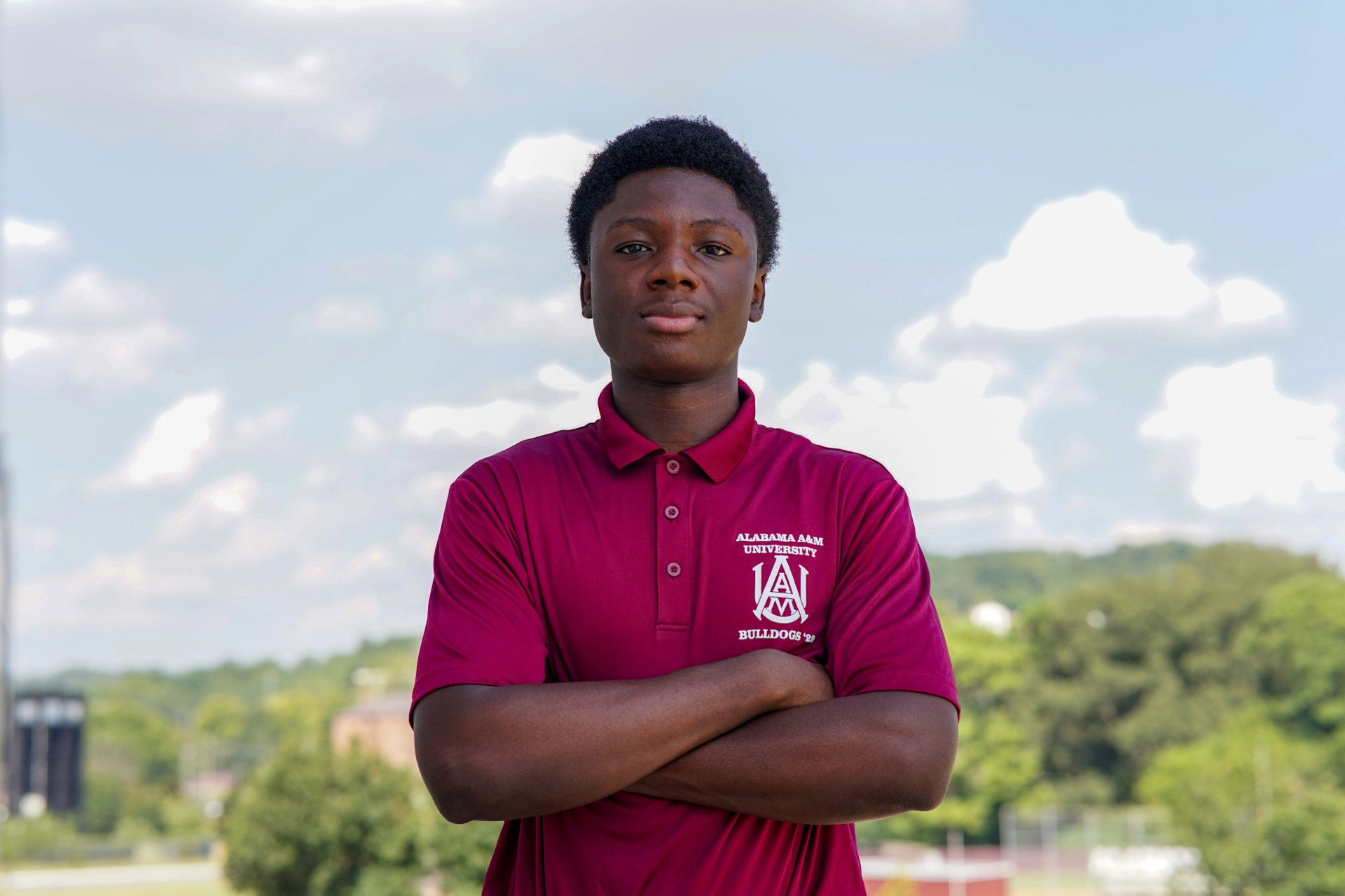 Samuel Oyediran stands with arms crossed with AAMU campus behind him