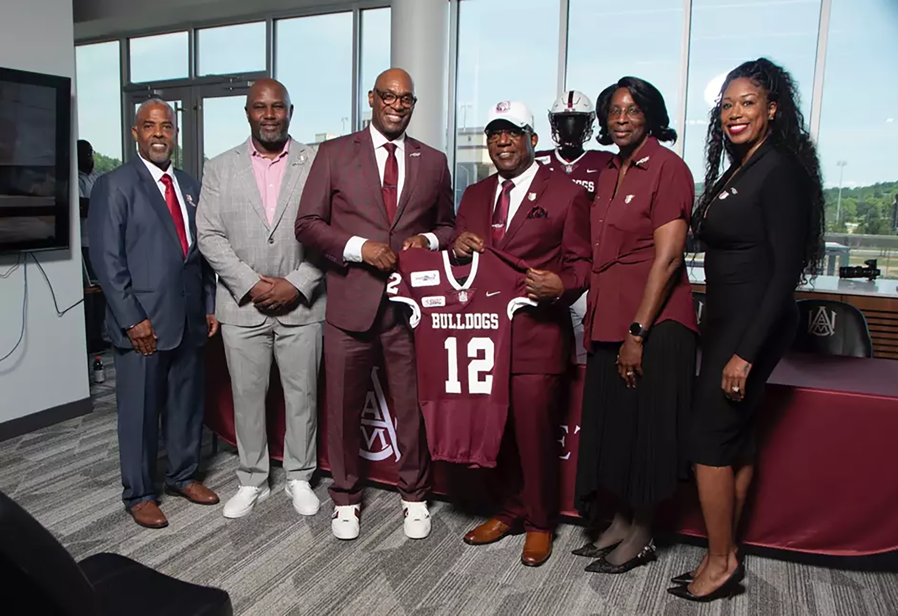 Alabama A&M Head Football Coach Sam Shade, second from left, and Director of Athletics Dr. Paul A. Bryant pose with a Bulldogs football jersey alongside four Alabama A&M Athletics staff members.
