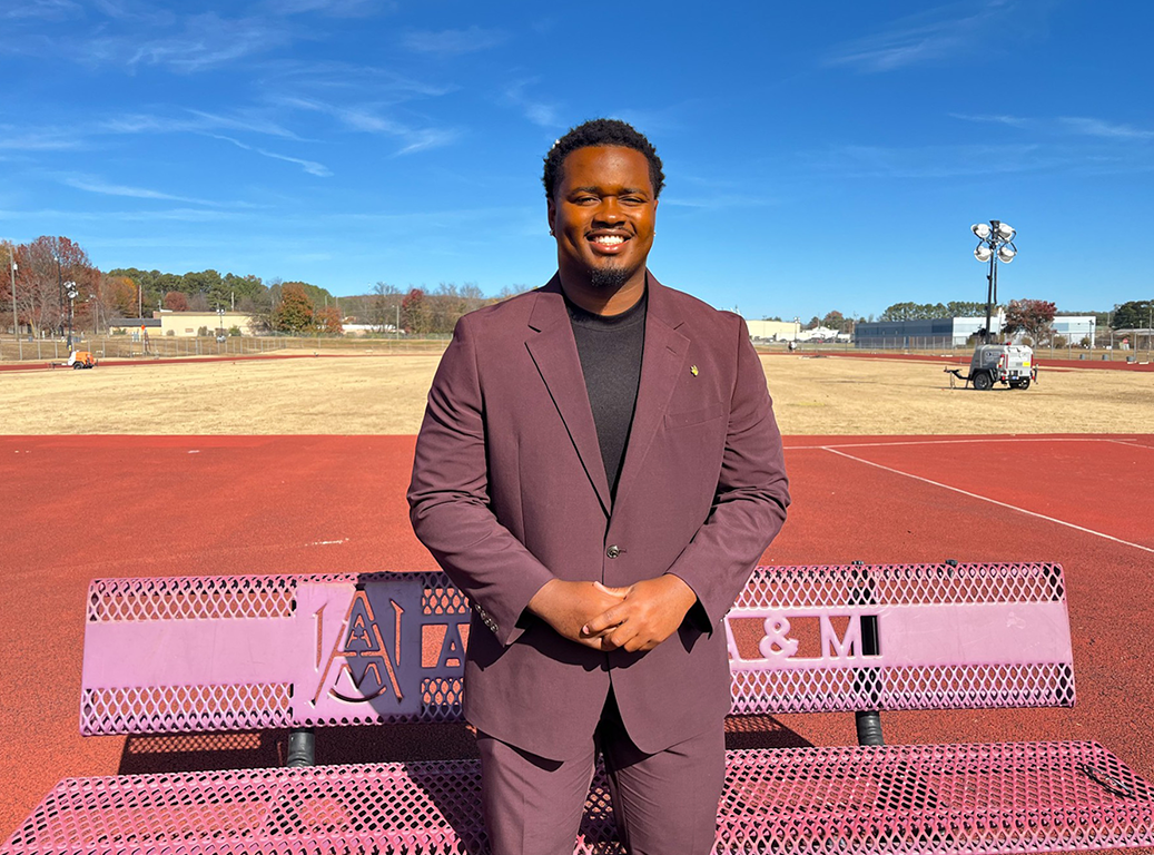 Preston London smiles while standing on the AAMU Track and Field practice field 