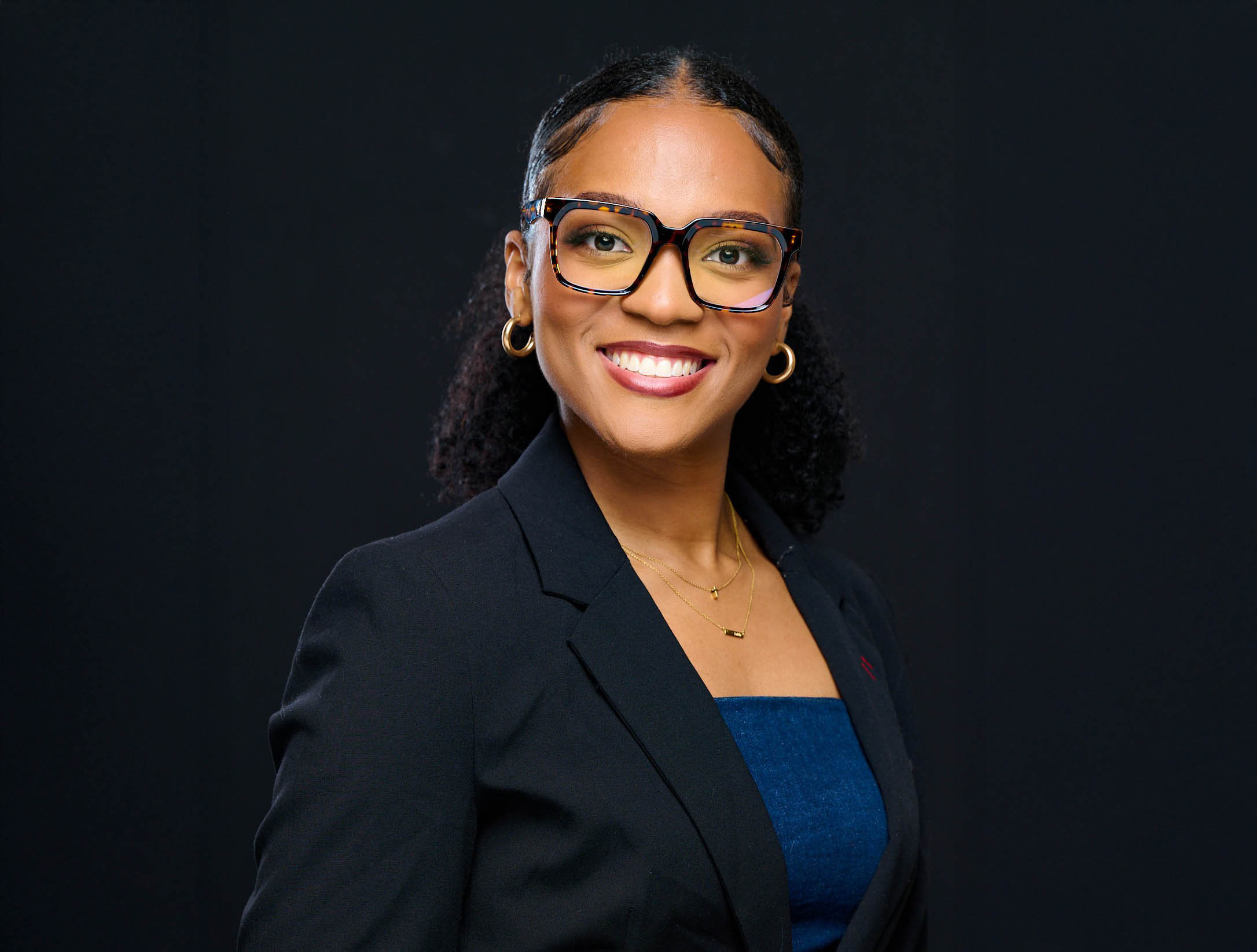 Rebecca Querin smiles at camera wearing glasses and dark business jacket