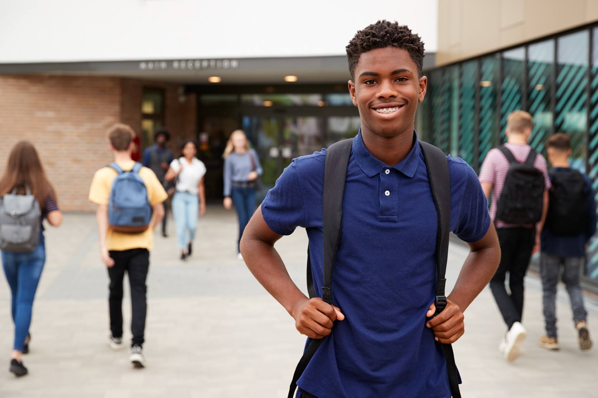 Student with backpack smiles at camera in front of a school