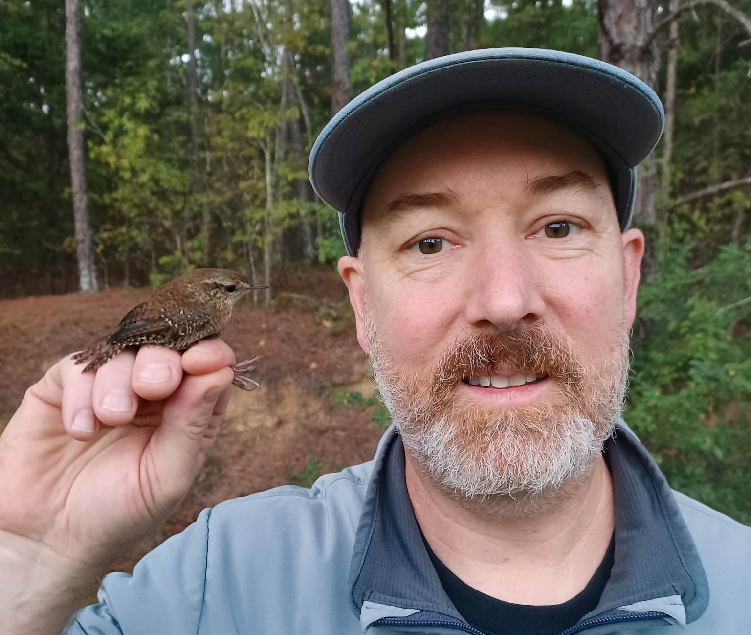 Ph.D. Student Thomas Thompson in the forest with a tiny brown bird sitting on his hand