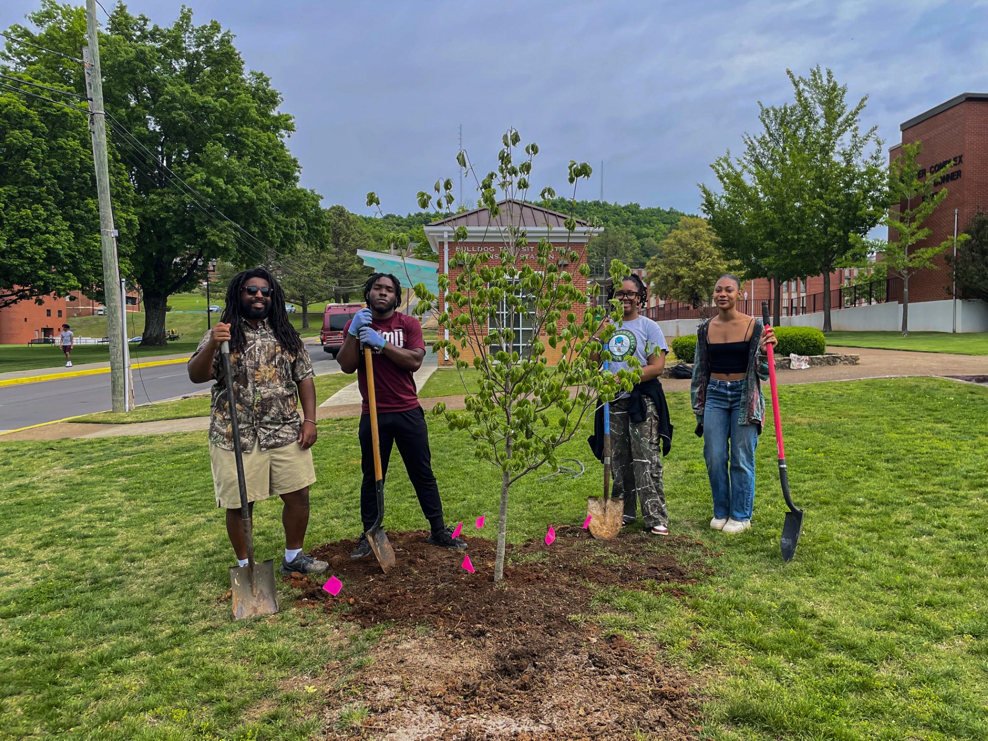 Four AAMU students stand with shovels behind tree they planted on campus