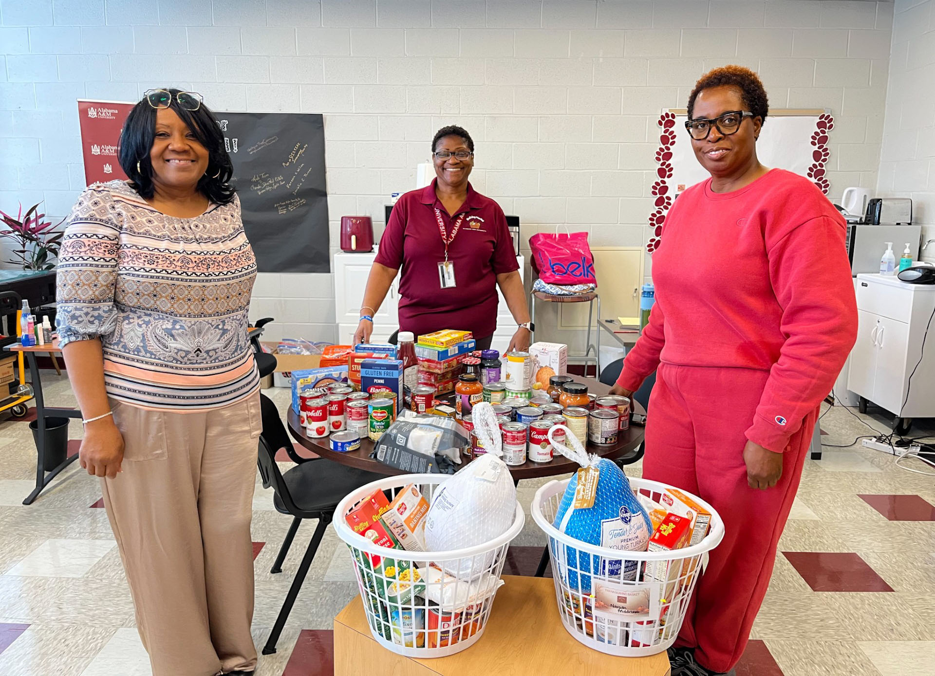 Monica Clarke, Lorelyn Swinton and Kawania Harris stand beside food donations and two turkey baskets for AAMU students