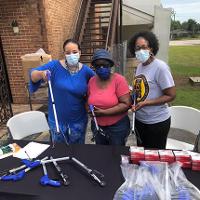 Three agents stand at a booth passing out grabber assistance devices to older adults.