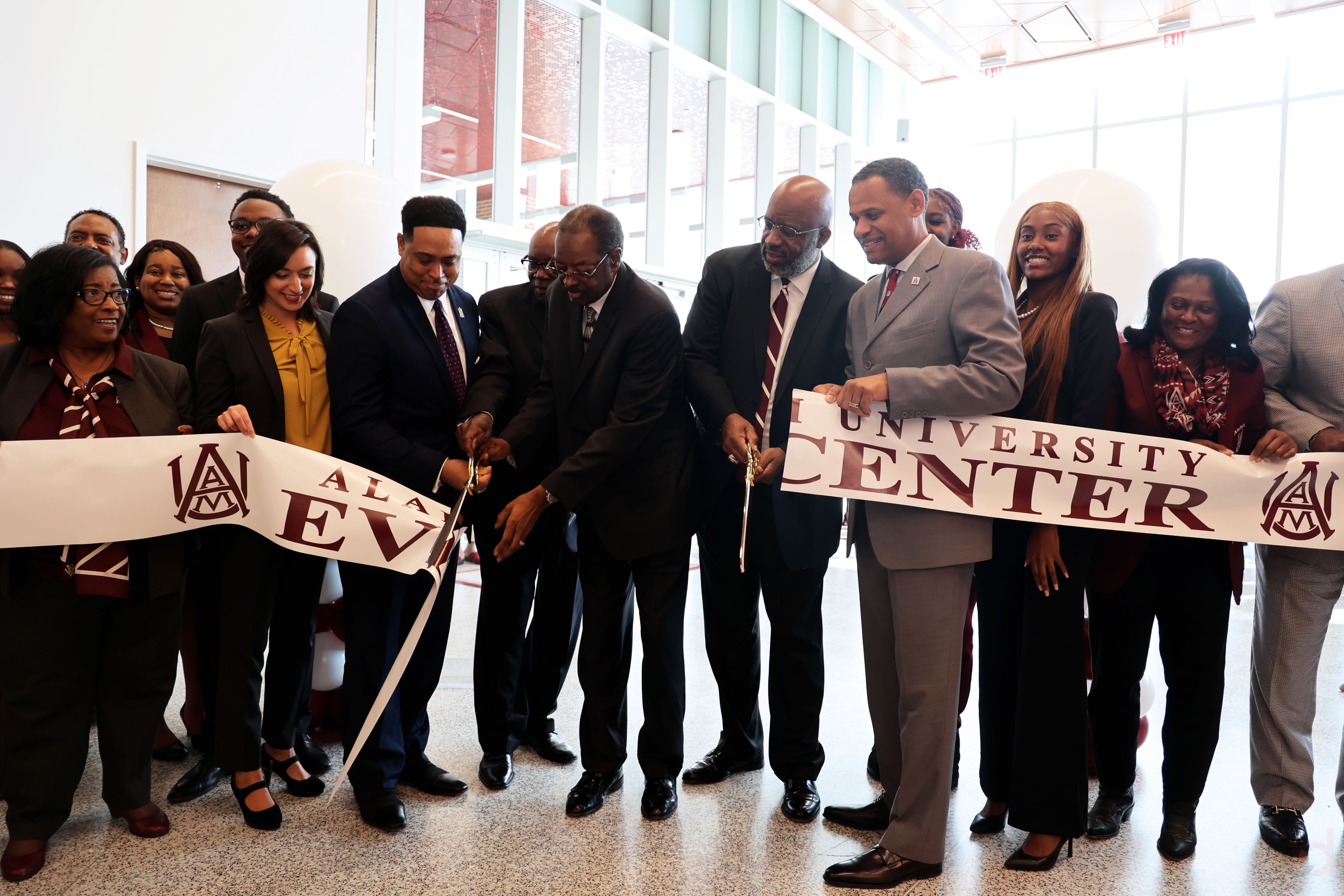 As a group of people in dress clothes look on, a main cuts a large ribbon for Alabama A&M's events center using oversized scissors.