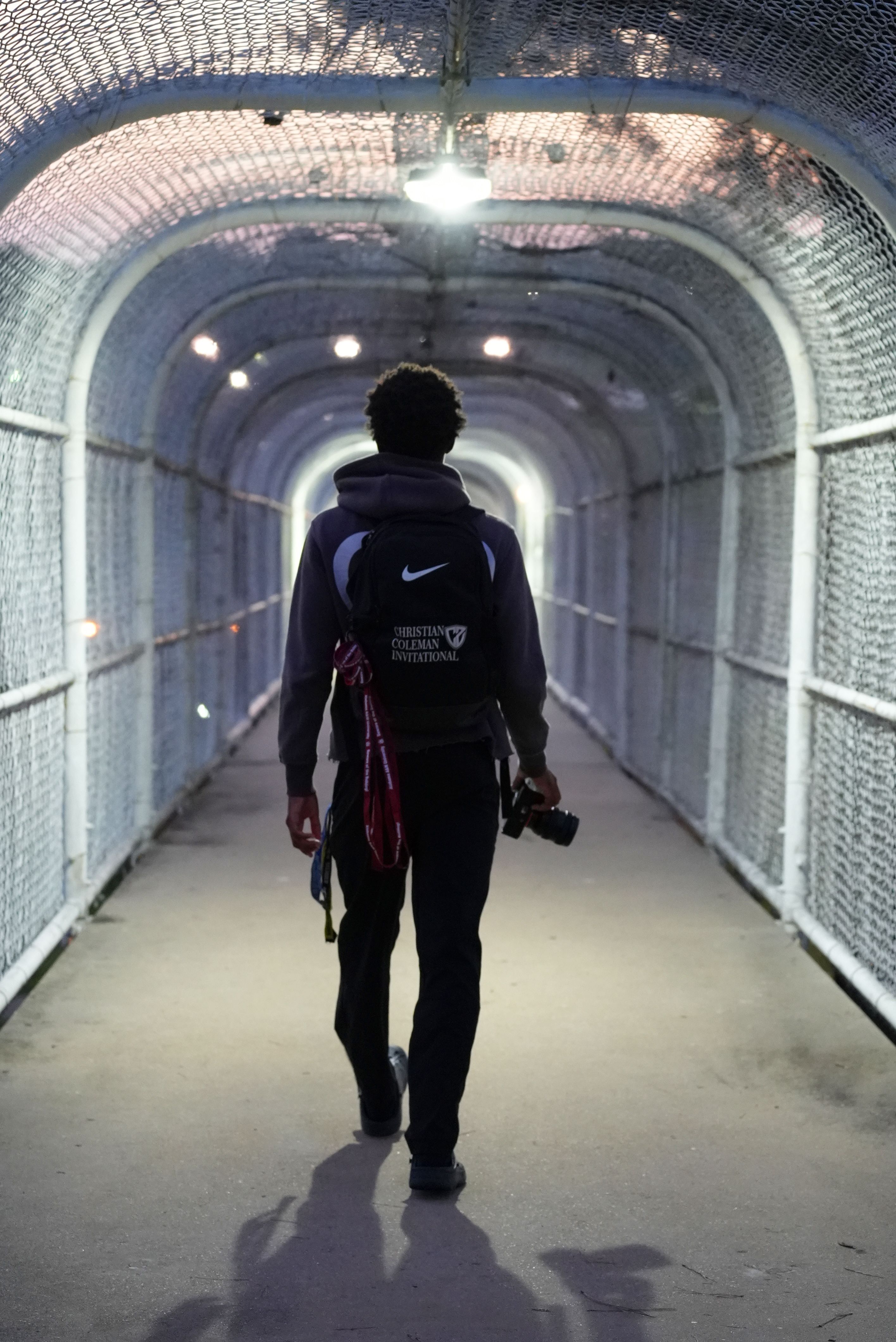 A student walking through a dramatically lit tunnel with camera in hand.
