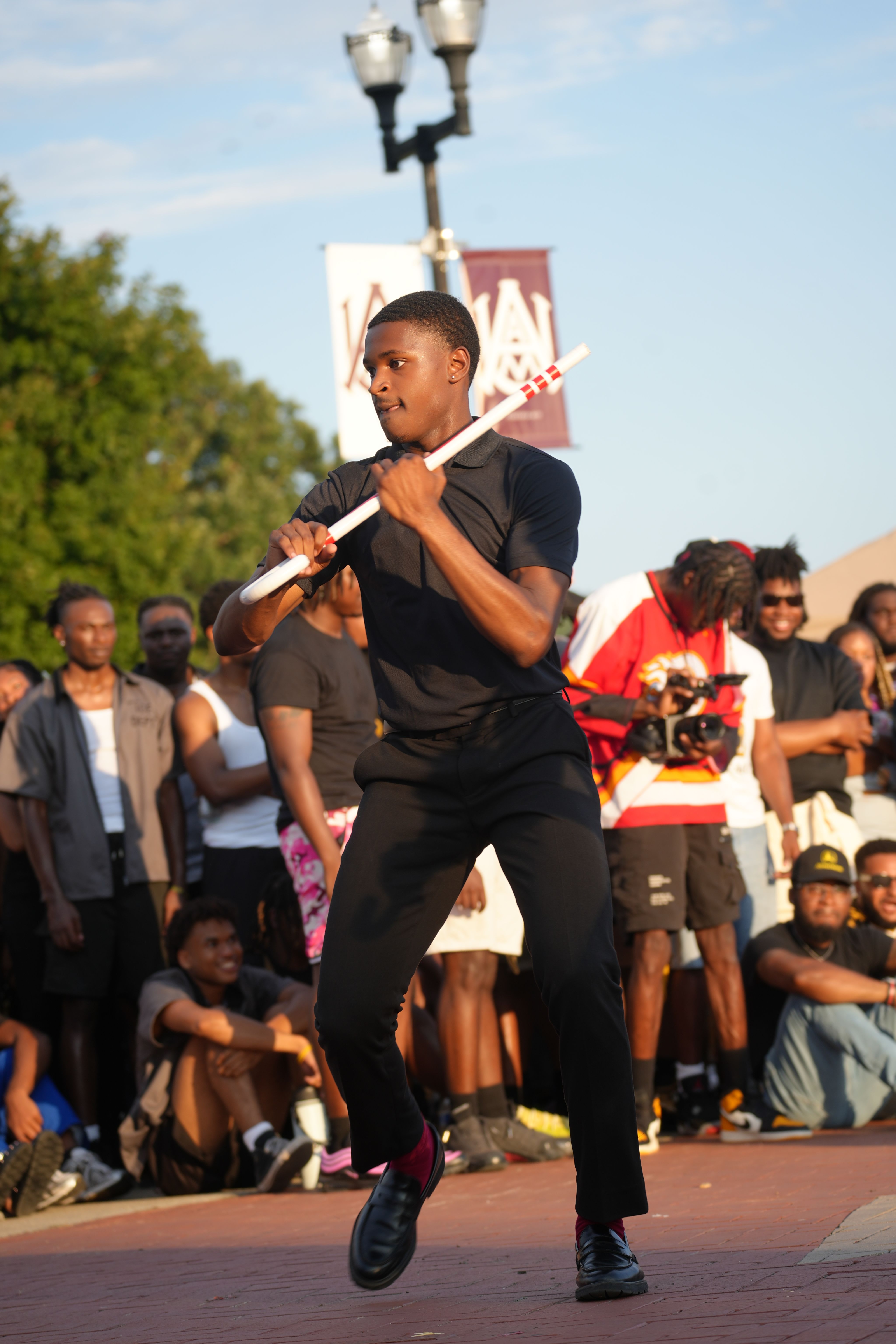 A student dancing on the sidewalk as a crowd looks on.