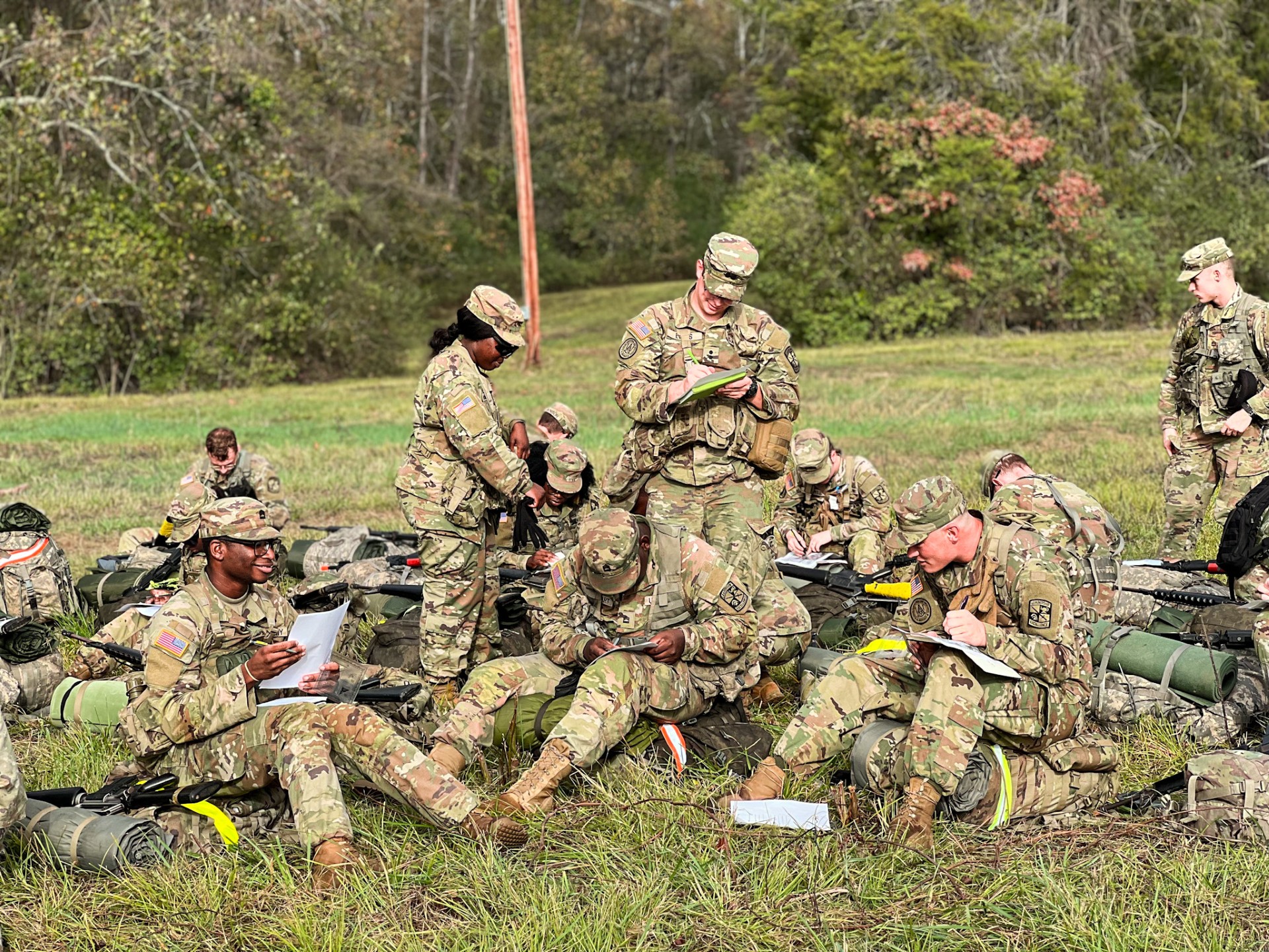 3 cadets standing and 8 sitting in a field looking at maps