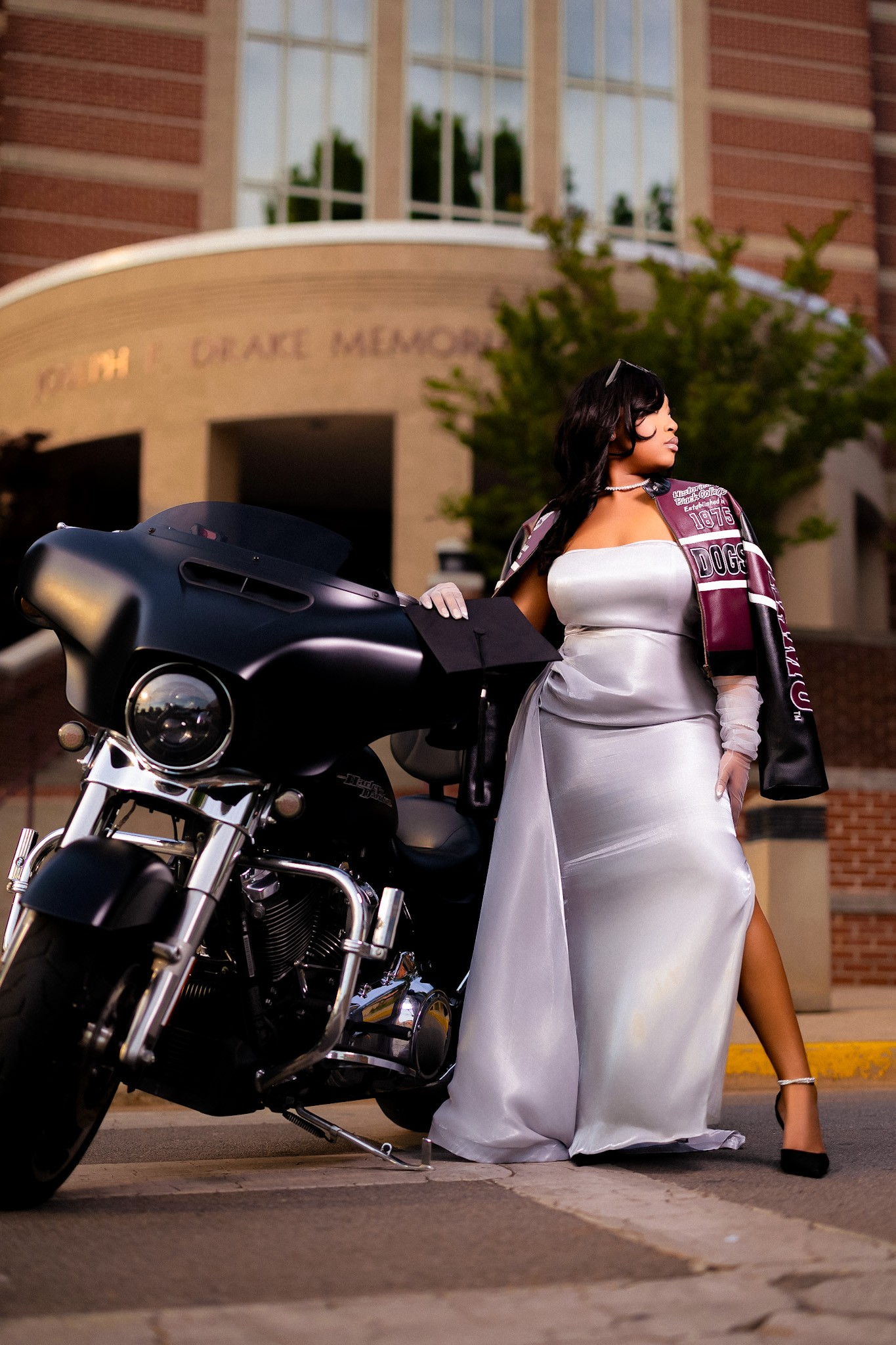 Jailyn Leonard in a shiny grey gown standing by a black motorcycle in front of the AAMU Library