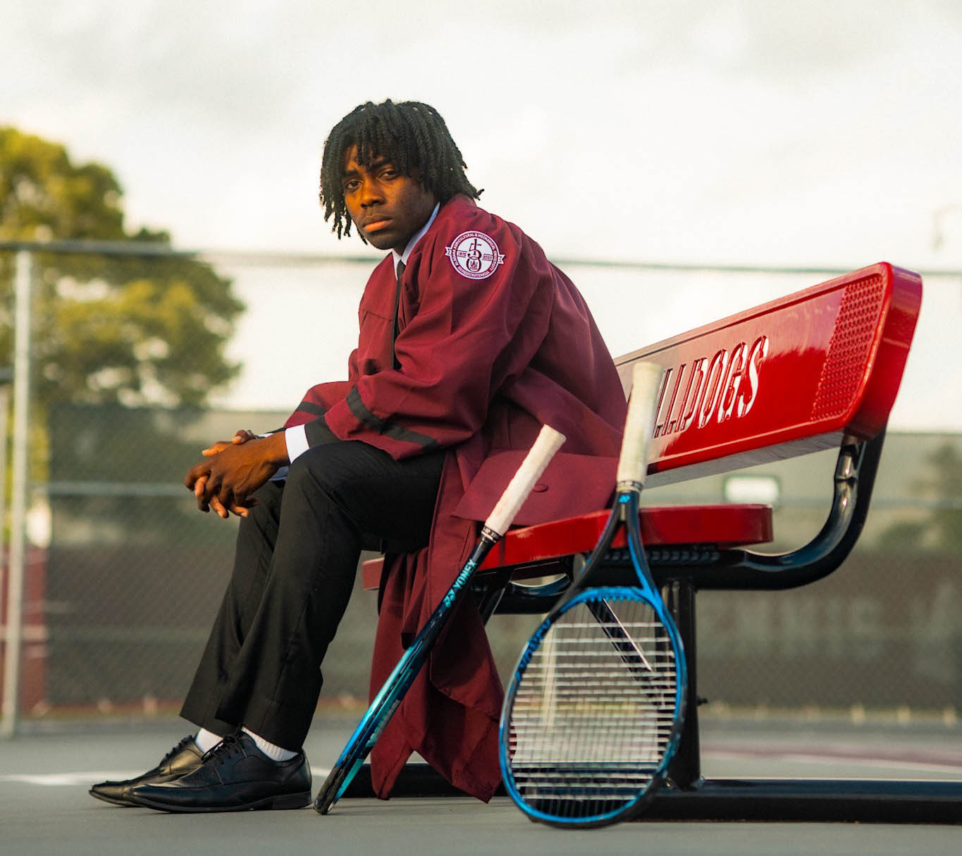 Lawrence wears his commencement robe while sitting in the AAMU Tennis Court with two rackets near him