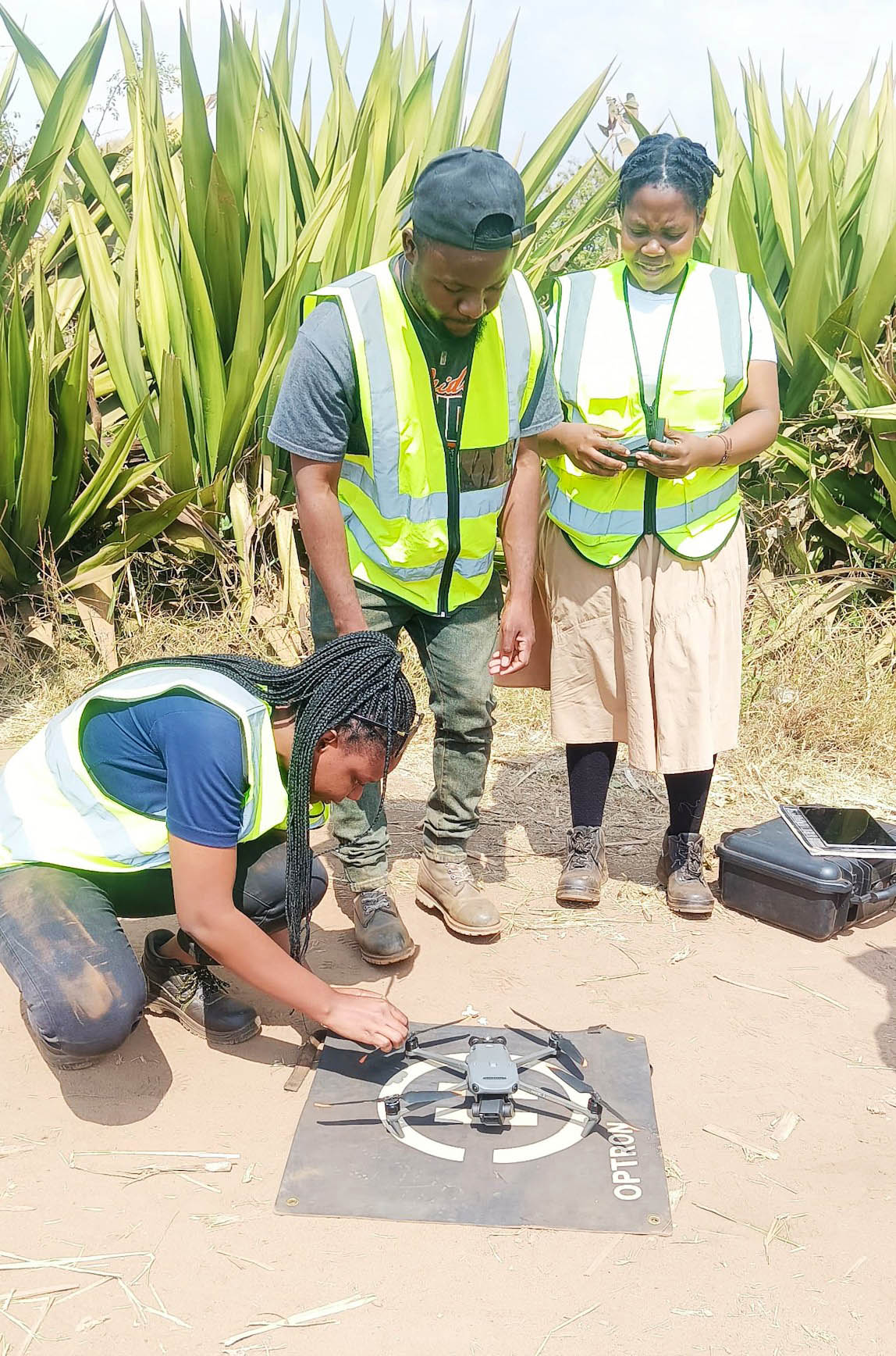 Kaunda works on a drone on the ground while two workers assist