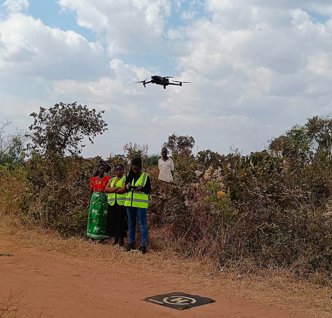Kaunda flying a drone with three colleagues standing nearby in a field
