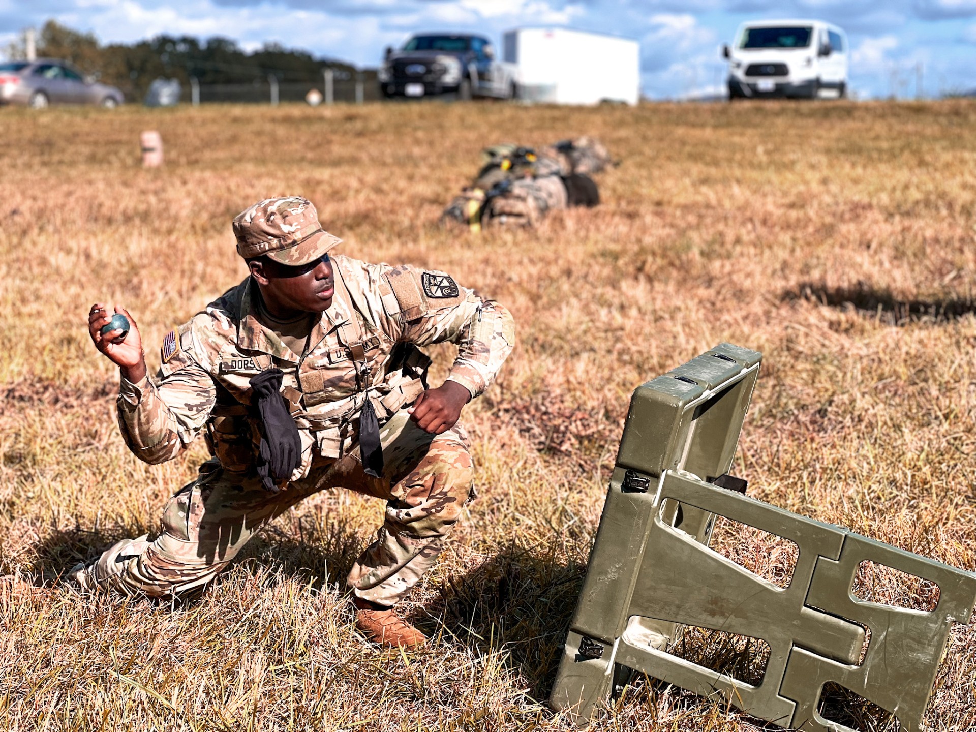 Cadet crouched in a field throwing a fake grenade