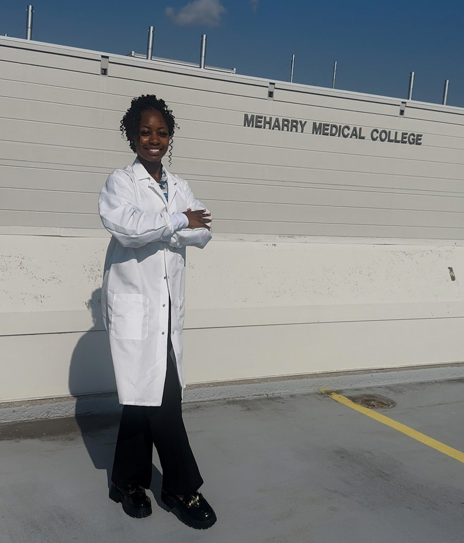 Ferguson wears lab coat and stands by sign that says Meharry Medical College