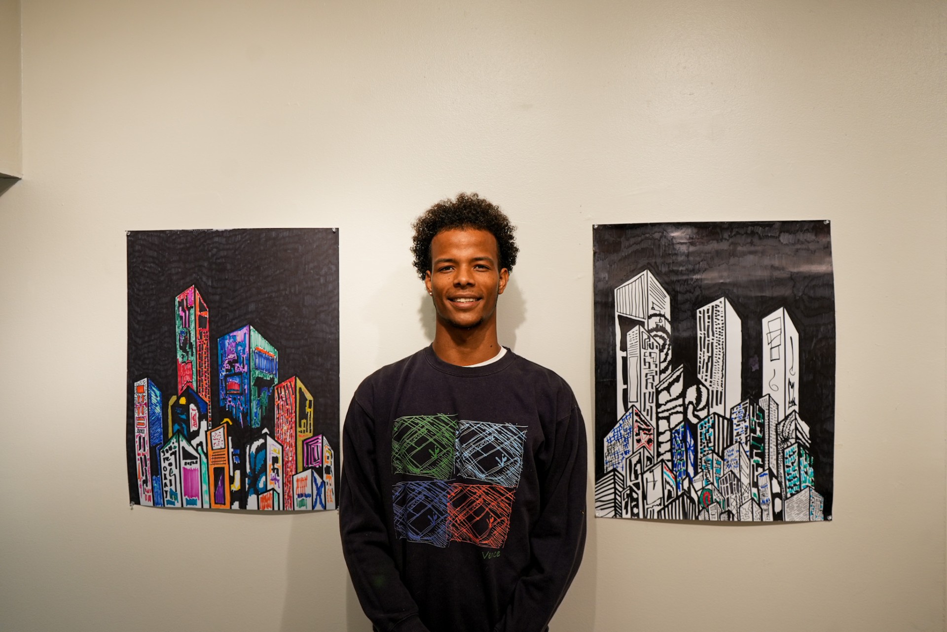 Vence N'tcha stands in between two of his artwork made with markers