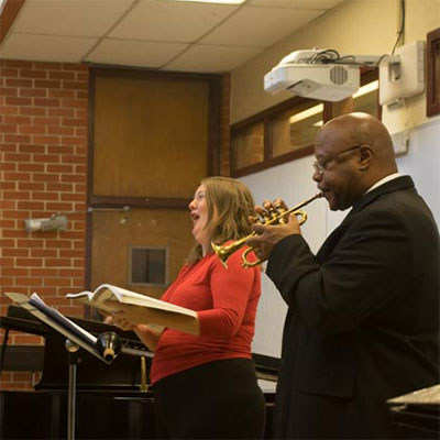 A woman sings as a man plays the trumpet