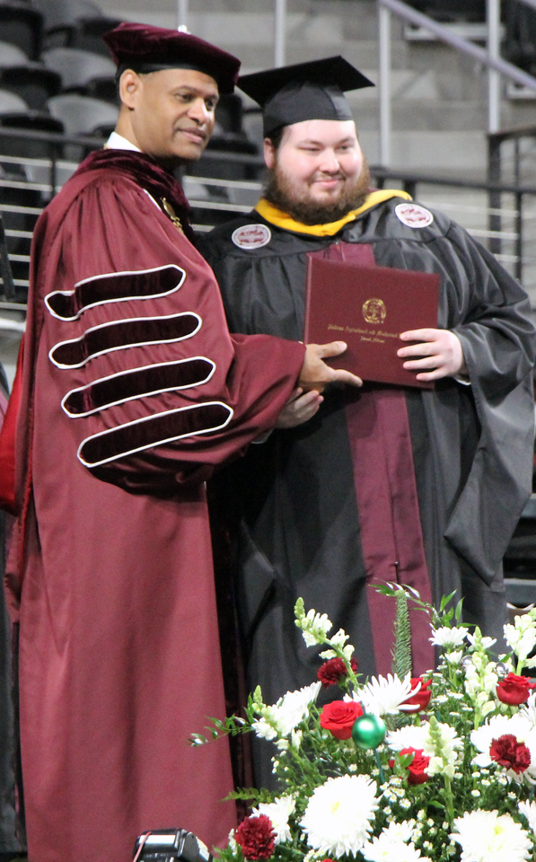 A smiling student receives her diploma from AAMU President Dr. Andrew Hugine