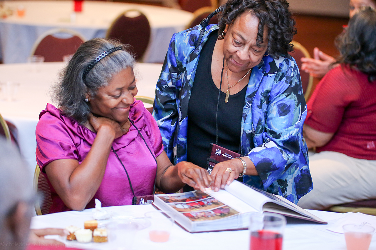 A photo of Alumni looking at photos from their preivous class reunion.